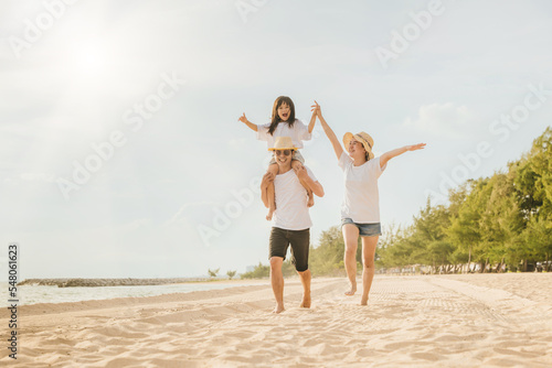 Family day. Happy family people having fun in summer vacation run on beach, daughter riding on father back and mother running at sand beach, family trip playing together outdoor, traveling in holiday © sorapop