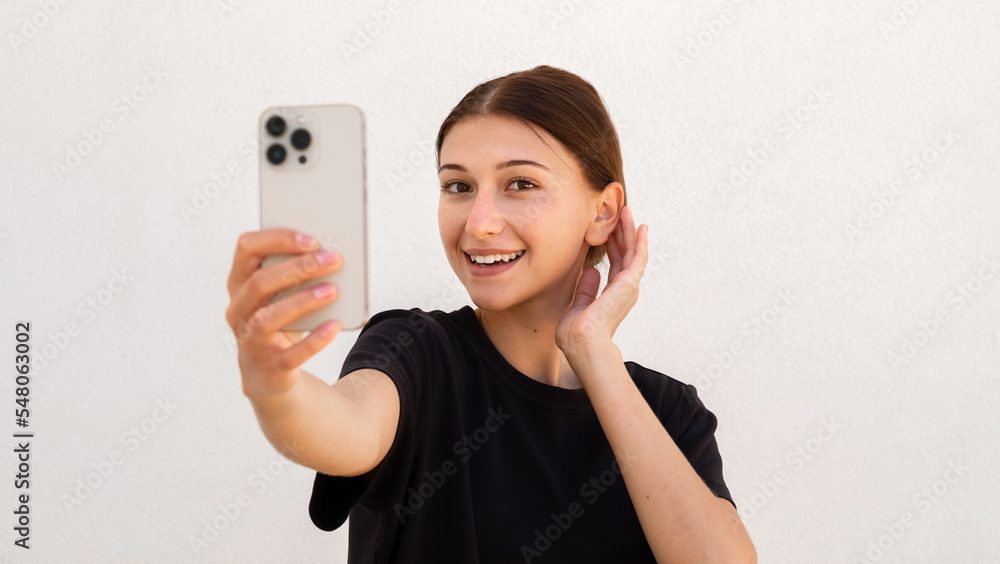 Portrait of happy young woman smarten up while looking at phone over white background. Caucasian woman wearing black T-shirt taking selfie or using mirror app. Mobile technology concept Portrait of happy young woman smarten up while looking at phone over white background. Caucasian woman wearing black T-shirt taking selfie or using mirror app. Mobile technology concept