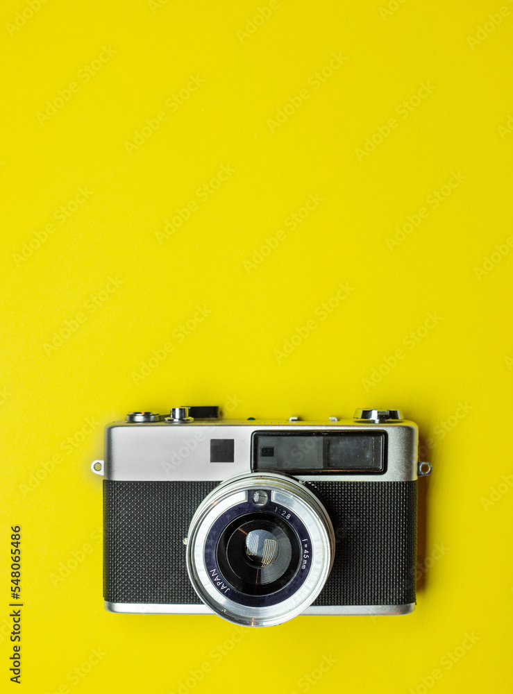 classic metalic analogic camera in silver and black colour. zenithal position. on a yellow background with texture. in vertical position. for use in social networks. space for copy. space for text