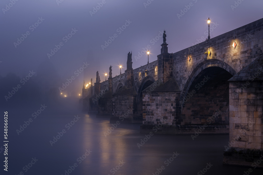 Charles bridge from below in the fog in the early morning in Prague with statues and lanterns on the bridge. Czech Republic.
