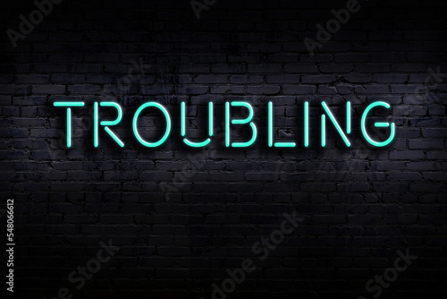 Neon sign. Word troubling against brick wall. Night view photo