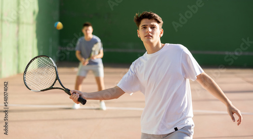 Caucasian young man serving ball during frontenis game outdoors. Boy playing pelota on outdoor fronton. © JackF