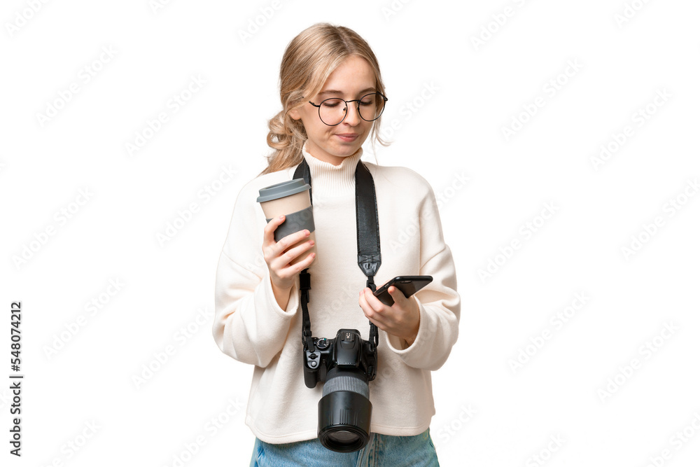 Young photographer English woman over isolated background holding coffee to take away and a mobile Young photographer English woman over isolated background holding coffee to take away and a mobile