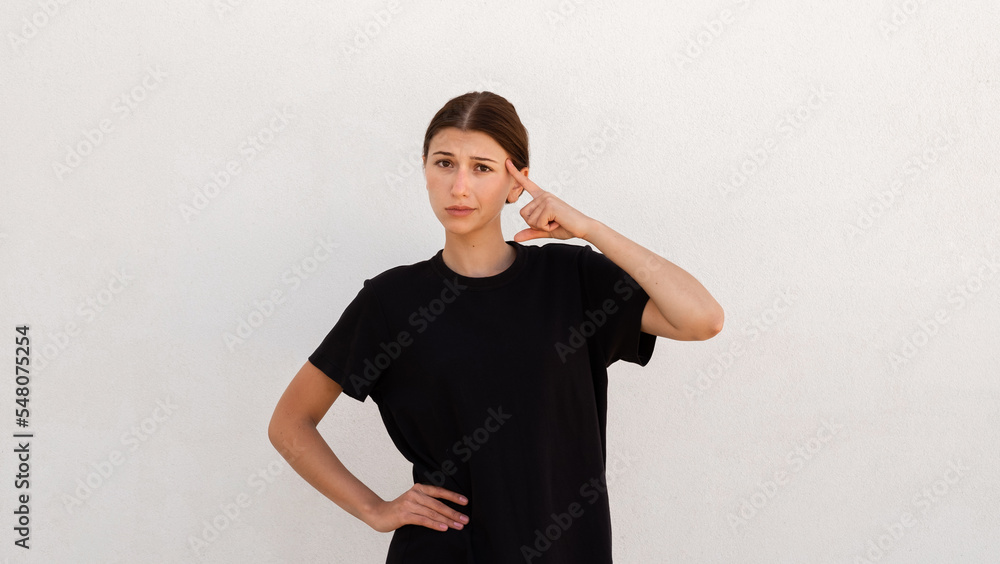 Portrait of serious young woman pointing at her head over white background. Caucasian woman wearing black T-shirt getting solution. Idea and creativity concept Portrait of serious young woman pointing at her head over white background. Caucasian woman wearing black T-shirt getting solution. Idea and creativity concept