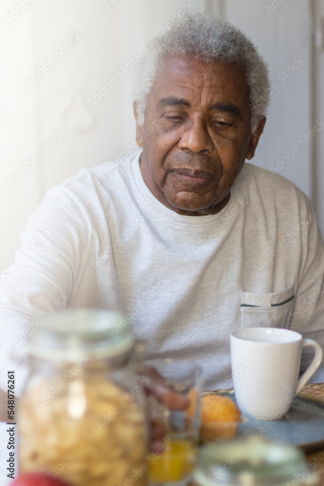 Portrait of elderly man having breakfast in morning. Thoughtful man in casual clothes calmly sitting at table with food on it drinking orange juice. Senior peoples life, support, health care concept Portrait of elderly man having breakfast in morning. Thoughtful man in casual clothes calmly sitting at table with food on it drinking orange juice. Senior peoples life, support, health care concept