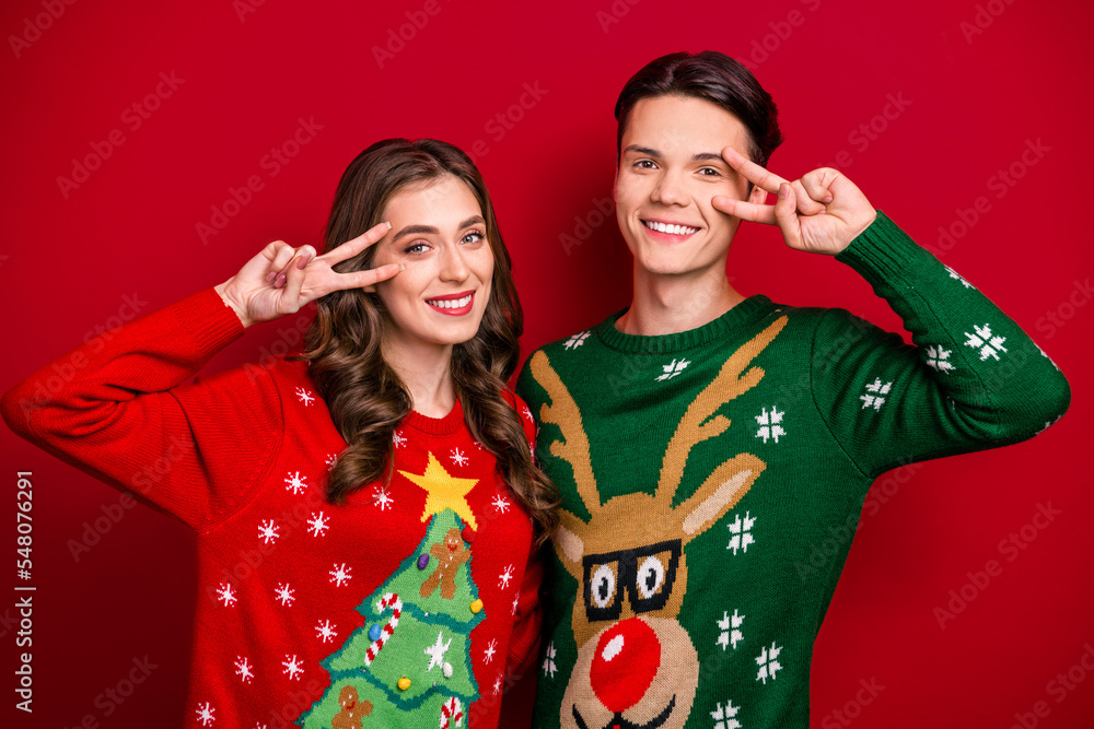 Photo of cheerful sister brother wife husband wear ugly sweaters show v-sign greetings symbol good mood isolated on red color background Photo of cheerful sister brother wife husband wear ugly sweaters show v-sign greetings symbol good mood isolated on red color background