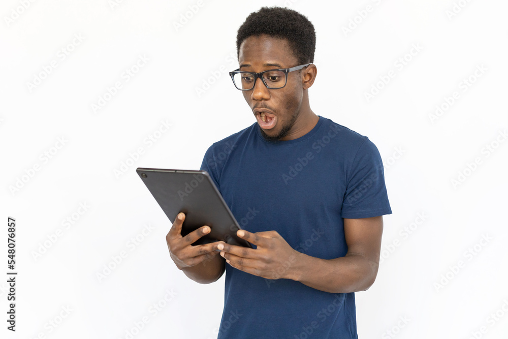Shocked man looking at tablet. Young African American male model seeing unexpected information on tablet. Portrait, studio shot, technology concept Shocked man looking at tablet. Young African American male model seeing unexpected information on tablet. Portrait, studio shot, technology concept