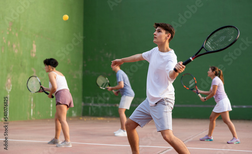 Young male pelota player hitting ball with racket during training game on outdoor Basque pelota fronton.