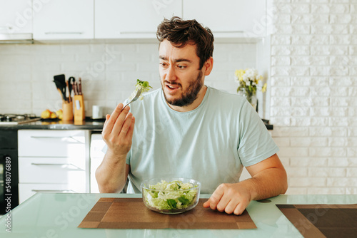 Fotografia Distraught with hunger, a young guy doomily eats a green salad
