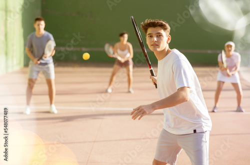 Athletic guy hits the ball with a racket while playing frontenis on outdoor court
