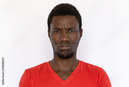 Closeup of displeased African American man frowning. Angry young male model with short dark hair in red T-shirt looking at camera, pouting lips. Anger, conflict concept