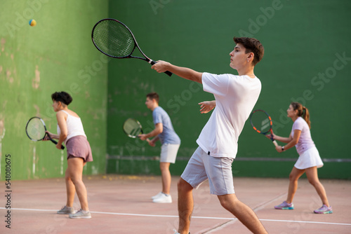 Young male pelota player hitting ball with racket during training game on outdoor Basque pelota fronton. © JackF