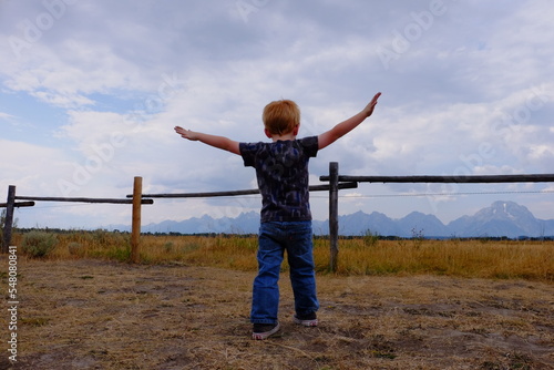 person standing with outstretched arms in front of a mountain range