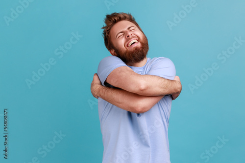 Fotografia Portrait of satisfied positive handsome bearded man embracing himself, closed eyes and smiling with pleasure, complacency and egoism