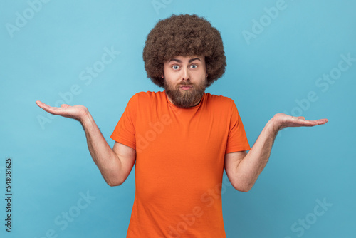 Slika na platnu Clueless confused man with Afro hairstyle in T-shirt shrugging shoulders as doesn't know answer, can`t make decision, being uncertain, not sure