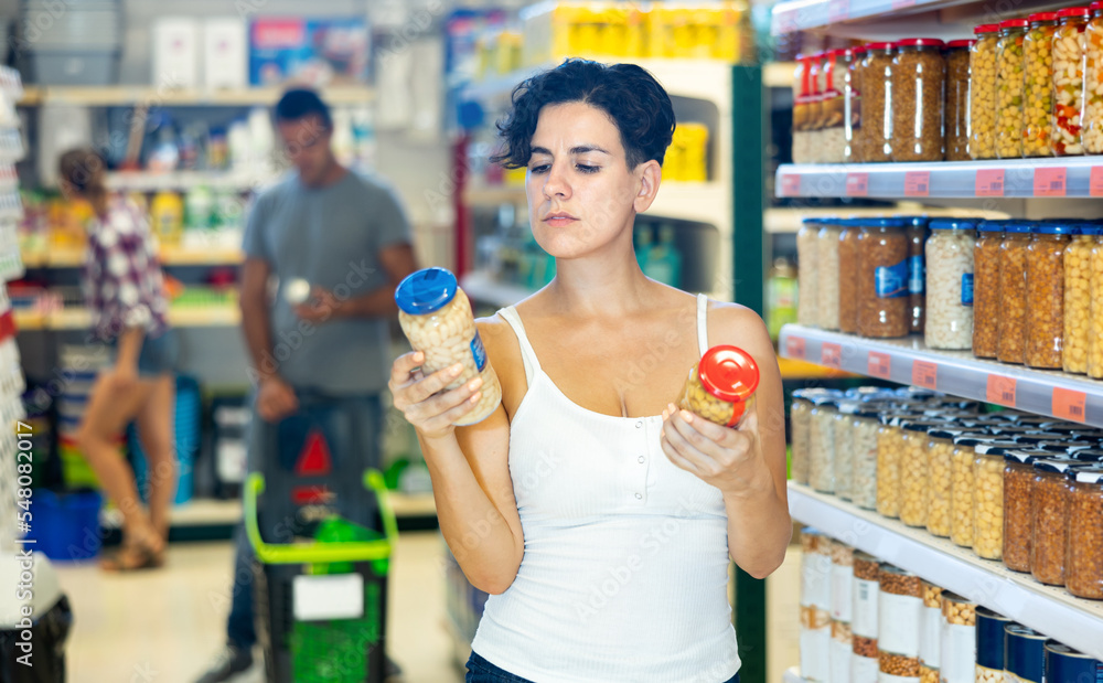 Smiling woman choosing jar of beans at the modern supermarket