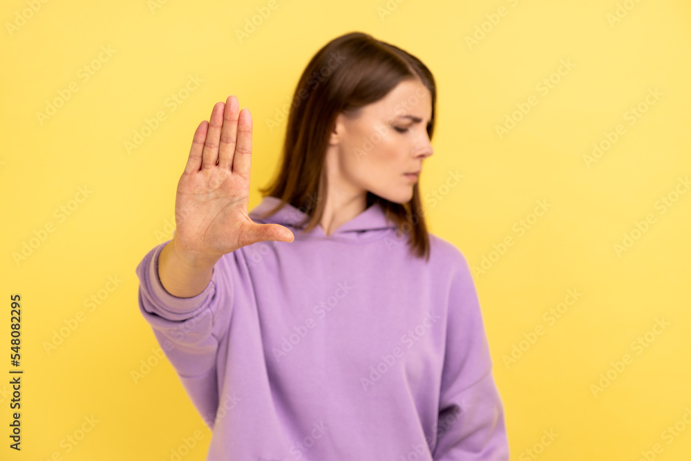 Frightened confused woman showing stop gesture with palm of hand, trying to stop abuser, rejection, afraid of domestic violence, wearing purple hoodie. Indoor studio shot isolated on yellow background Frightened confused woman showing stop gesture with palm of hand, trying to stop abuser, rejection, afraid of domestic violence, wearing purple hoodie. Indoor studio shot isolated on yellow background
