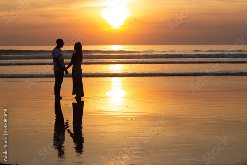 Tender family walking on beach at sundown. Man and woman in casual clothes strolling near water at dusk. Love, family, nature concept