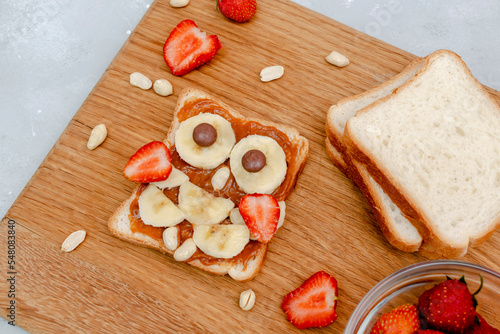 Funny owl face sandwich toast bread with peanut butter, banana, strawberry on wooden board. Cute kids childrens baby's sweet dessert, healthy breakfast,lunch, food art on gray background,top view