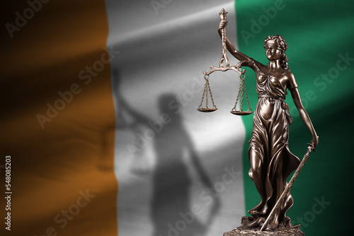 Ivory Coast flag with statue of lady justice and judicial scales in dark room. Concept of judgement and punishment photo