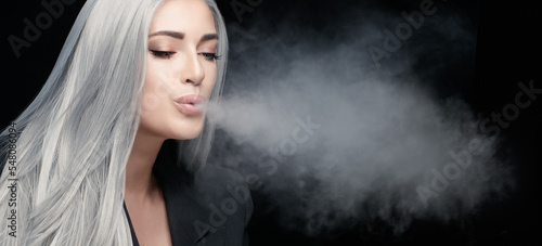 Vaping concept. Gorgeous vaper woman blowing a big steam cloud in a panorama banner isolated on black background with copyspace
