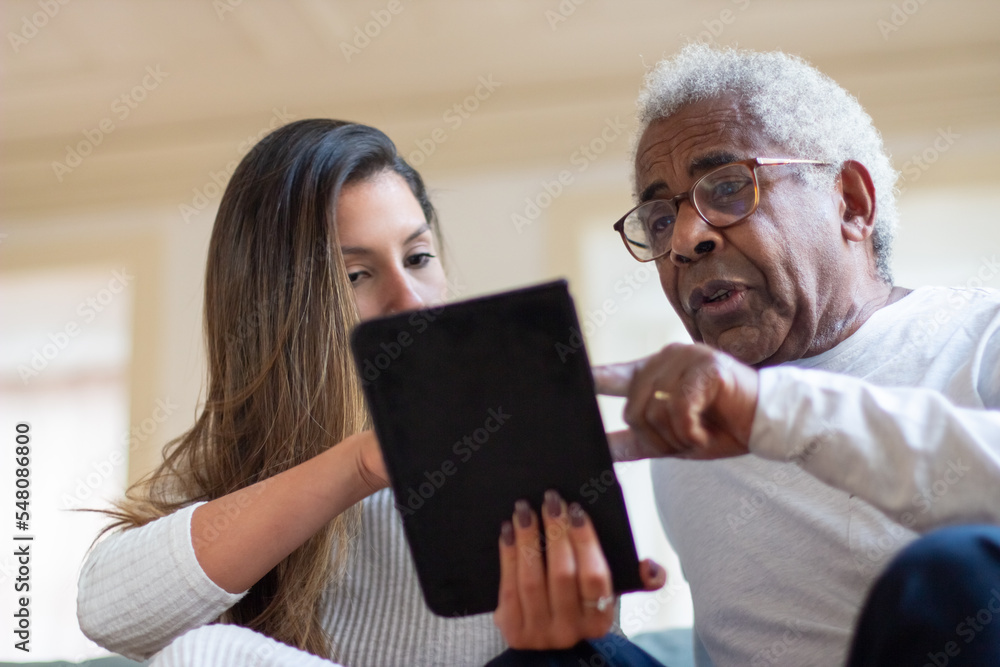 Close-up of aged man and daughter with digital tablet. Happy old man resting at home and young woman explaining how to use tablet for internet. Taking care of old people, modern technologies concept Close-up of aged man and daughter with digital tablet. Happy old man resting at home and young woman explaining how to use tablet for internet. Taking care of old people, modern technologies concept