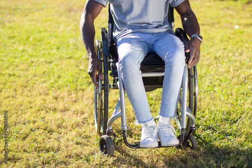 Closeup shot of Black man sitting in wheelchair in park, enjoying riding on green lawn on sunny evening in city park. Disability, leisure time, motivation concept.