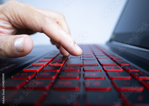 Male hand about to press the enter key on a laptop keyboard, with red lighting. (selective focus of the subject or point of action intentionally)