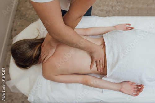 Woman lying face down on massage table and enjoying remedial body massage done by professional masseur in spa salon