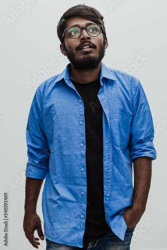 Indian smiling young man with blue shirt and glasses posing on gray background