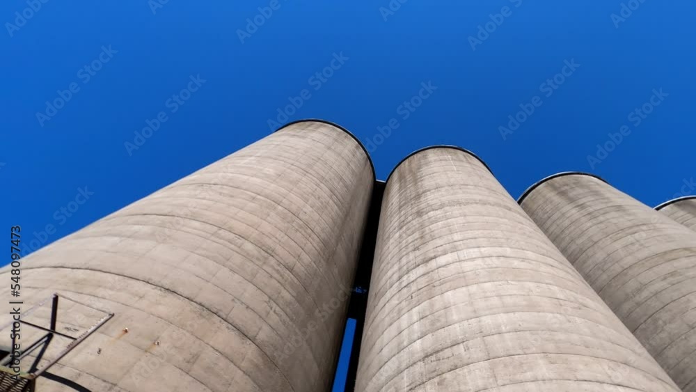Looking up along surface of multiple large concrete silos under clear blue sky, rotate; in Ontario, Canada. Looking up along surface of multiple large concrete silos under clear blue sky, rotate; in Ontario, Canada.