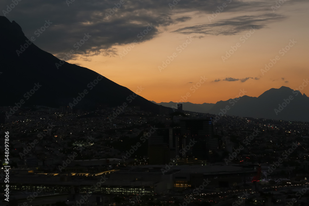 Picturesque view of sunset with dark clouds above big mountains and evening city