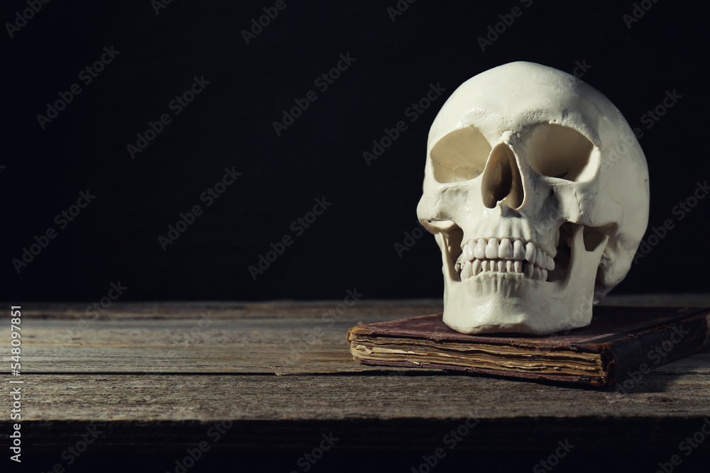 Human skull and old book on wooden table against black background, space for text Human skull and old book on wooden table against black background, space for text