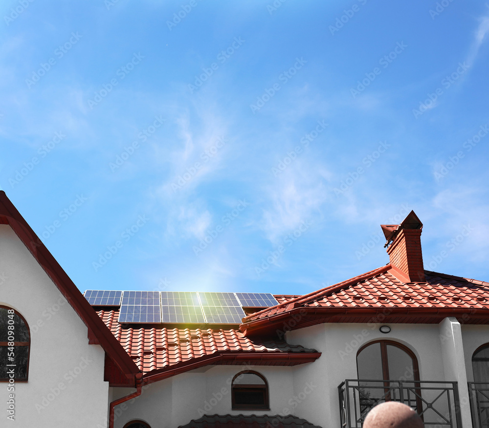House with installed solar panels on roof under blue sky. Alternative energy source House with installed solar panels on roof under blue sky. Alternative energy source