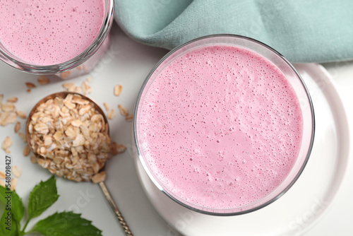 Glasses of blackberry smoothie and oatmeal on white table, flat lay