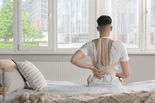 Fotografía Man with orthopedic corset sitting in room, back view