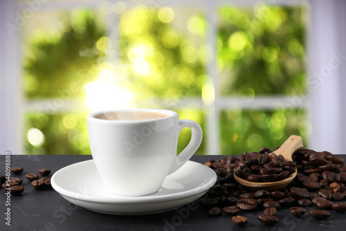 Cup of aromatic coffee and beans on grey table indoors