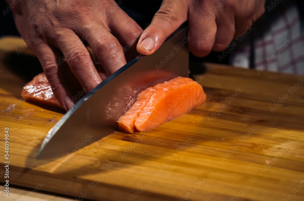 Close up of Chef cook hands chopping salmon fish for traditional Asian cuisine with Japanese knife. Professional Sushi chef cutting seafood japanese chefs are making salmon fish sashimi. dark tone