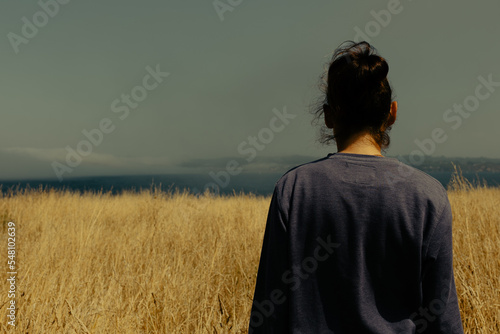 The girl from behind looks at the sea in the fog. A girl stands in a field of yellow grass or wheat. © Pablo Santos Somos