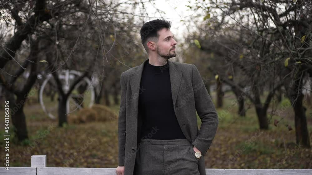 Zoom in to confident young millennial man checking time on watch smiling waiting for a meeting outdoors. Front view portrait of Caucasian guy in autumn park leaning on wooden fence looking around Zoom in to confident young millennial man checking time on watch smiling waiting for a meeting outdoors. Front view portrait of Caucasian guy in autumn park leaning on wooden fence looking around