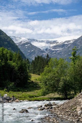 Vertical shot of a river and greenery in front of Buarbreen glacier mountain under blue cloudy sky photo