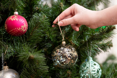 Christmas mood, holiday atmosphere. A girl hangs a Christmas ball on a Christmas tree.