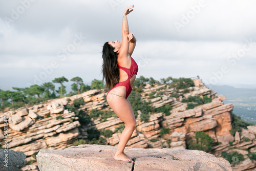 Caucasian long-haired mature woman exercising on mountain summit barefoot and scantily clad