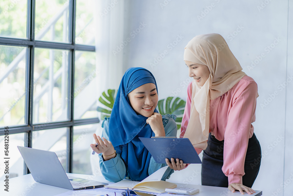 Two young modern muslim women working and discussing work in business meeting at meeting room with financial graphs and laptop