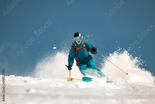 Fast male skier rides downhill over ski slope and throws a lot of snow