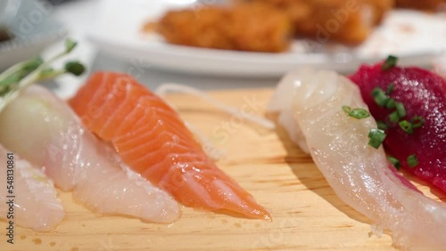 Person uses chopsticks to select piece of salmon sushi from serving board. photo