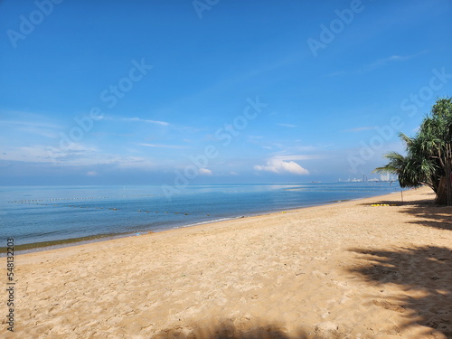 Sunlit beach with tree shade on the sand. Calm sea  bright blue sky  white clouds  sea without waves  suitable for relaxation. 