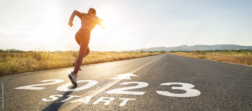 New year 2022 or start straight concept.word 2022 written on the asphalt road and athlete woman runner stretching leg preparing for new year at sunset.Concept of challenge or career path and change. - obrazy, fototapety, plakaty 