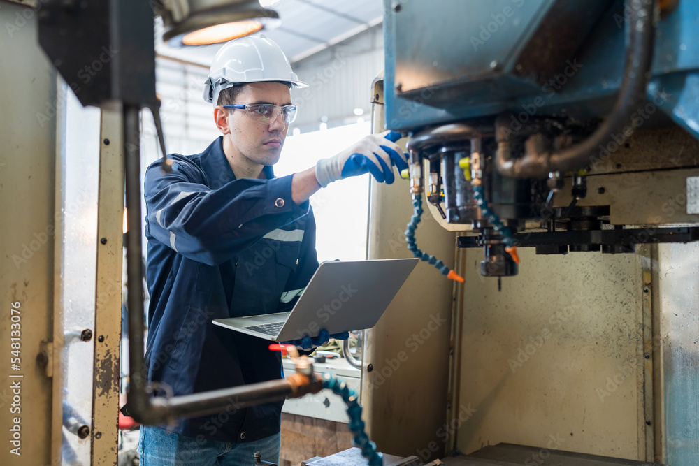 Male engineer worker working with laptop computer for control machine in the workshop. Male worker working with lathe machine with safety uniform, goggles and helmet in the industry factory