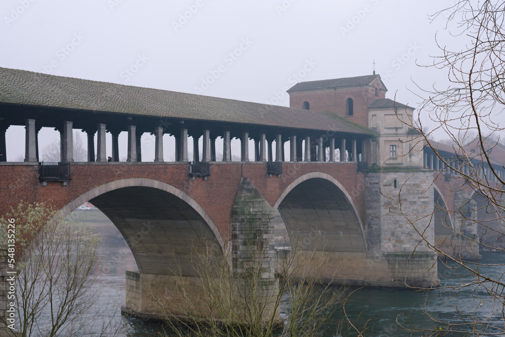 Ancient covered bridge surrounded by fog in winter. Pavia. Italy